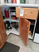 Open cabinet showing stainless steel pots and pans with black handles on shelves.