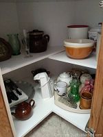 Corner shelf with brown bean pots, glass vase, mixing bowls, tea pots, and kitchen tools including knife block and can opener