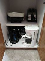 Shelf with electric kettle and white drip coffee maker with glass carafe
