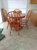 Side angle view of the round solid oak dining table and four spindle-back chairs around it.