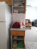 Overview of stacked folded towels (tea towels, hand towels) with white wall clock and a small figurine on the counter near refrigerator and shelves with more folded towels.