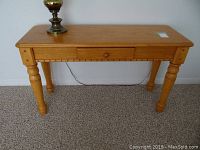 Front view of oak sofa table with lamp on top, showing turned legs and wood grain finish.