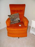 Front view of an orange vintage upholstered swivel rocking chair with a multicolor decorative pillow.