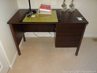 Front view of small laminate desk with decorative items, lamp, and books on top showing desk surface and drawer configuration.