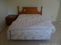 Front view of double mattress set on metal frame with floral pattern and oak headboard, bedspread covering mattress.