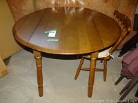Maple round drop leaf table with two armless chairs, showing table surface with stickers and join lines of drop leaves