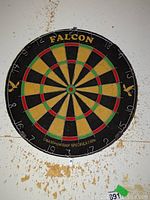 Front view of Falcon branded dart board with visible numbers, colored segments, and championship specification text