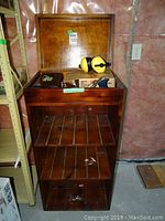 Wooden storage cabinet open showing contents including ear defenders, boxed propane torch starter kit, and hand plane.