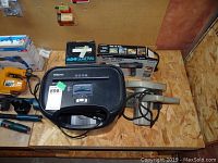 View of miscellaneous tools on wooden surface including a black Fellowes P-45C paper shredder, Mini General pump box, two electric heat strippers in front of boxes, and a yellow electric circular saw.