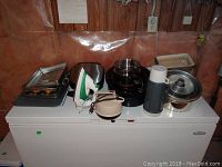 Overview of various baking pans, roast pans, kitchen appliances, and cookware on top of a white freezer or fridge.