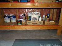 Shelf with various paint cans including Dulux Xpert and smaller containers of maintenance chemicals like oil and degreaser