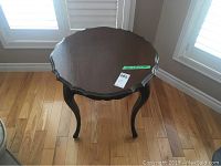 Round wooden side table viewed from above, showing scalloped edges and smooth dark wood finish.