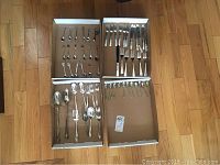 Full overview showing four trays containing various silver plated cutlery including forks, knives, and spoons, plus collector spoons with decorative handles.