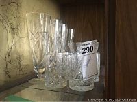 Photo showing a group of various crystal glasses arranged on a shelf including tall stemmed glasses, short stemmed wine glasses, and tumblers with pinwheel cut pattern.
