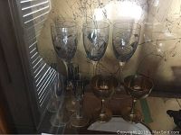 Photo showing 3 tall wine glasses with black spiral design, 2 silver plated wine glasses, and 4 shot glasses behind them