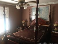 Full view of the four poster bed in a bedroom setting showing carved posts and headboard with dark bedding.