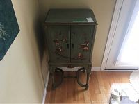 Front left angled view of the green wooden cabinet showing floral and scenic design on the front.