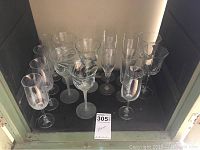 Photo of multiple wine glasses arranged inside a cabinet showing various styles of stems and bowls including swirled glass and frosted stems.