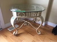 Front and side view of glass top table with decorative metal base showing scrollwork and design details.