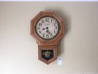 Full view of the wall clock mounted on a pale wall showing the wooden octagonal frame and pendulum compartment with 'Standard Time' text.