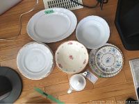 7 white dinner plates with gold trim, matching platter, serving bowl, decorative floral bowls, and Royal Doulton white teapot arranged on floor.