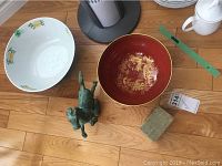 Photo showing white Spode-style bowl with yellow flowers, black bowl with gold design, metal horse figurine, and marble base on wood floor