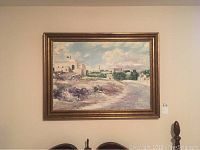 Front view of framed print artwork on a beige wall showing the landscape scene and wood frame.