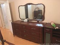 Front view of wooden triple dresser with attached mirror showing design, drawer handles, and mirror frame.