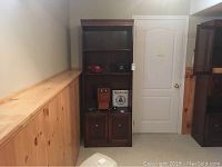 Full view of the wood bookcase showing two shelves and two doors on the bottom cabinet section, placed in a basement room.