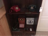 Two rotary dial phones on top shelf with wooden wall phone and Bell Telephone sign on bottom shelf, showing full collection arrangement.