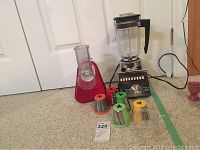 Full view of the Osterizer Cyclomatic blender on the floor with glass blender pitcher and multiple color-coded slicing cones arranged nearby.