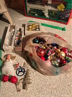 Photo showing various vintage glass Christmas ornaments and resin tree toppers arranged on carpet, including an angel topper and boxed sets of small gold ornaments.