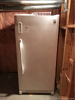 Front view of closed white Kenmore upright freezer in basement setting