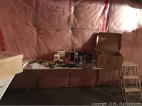 Box of assorted cords, painting supplies on the table, step ladder in background