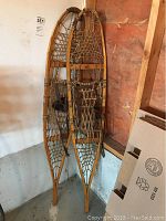 Full view of the pair of wooden snowshoes leaning against the wall in a storage area.