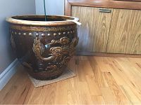 Full view of large dark brown ceramic planter with raised dragon and decorative motifs around the exterior, sitting on wooden floor with woven mat underneath.