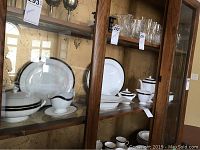 View of several pieces including covered bowls, gravy boat, large plates in a wooden cabinet with glass doors.