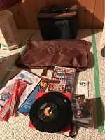 Knitting needles, records, tapes, DVD, garment bag and travel case arranged on floor