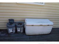 Photo showing two gray paint buckets and a large white Igloo cooler placed on the ground against a wall.