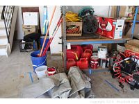 Wide view showing milk crate with yellow outdoor power cords, red plastic gas cans, paint cans, paint rollers in bucket, tarp on floor, and shelving with additional items.