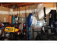 Fishing rods and other outdoor gear stored in garage: multiple rods with reels, additional rods, and nets hanging on wooden beam.