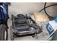 Front angle of Craftsman gas mower showing handlebar, wheels, and part of the engine with a bag of gardening product nearby.
