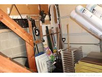 Wide view of garage corner showing garden tools, wooden dolly, pet crate and vent covers stacked.