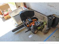 Wide photo of the lot showing the plastic case with chain saws, boots, hip waders, and lubricant bottle on concrete floor in a garage.