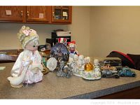 Overall view of the lot items arranged on a counter: figurines, dolls, snow globe, cars, plate, and pewter pieces