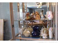 Display case shelf showing two Sadek porcelain birds on wood bases, two Virgin Mary busts, bird figurines, and ceramic/clear vases in background