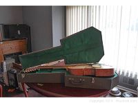 Handmade 12-string acoustic guitar resting in open custom green lined hard case on wooden table.