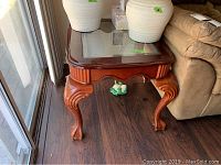 Photo of one wooden end table showing claw and ball feet, beveled glass top, and carved wooden sides.