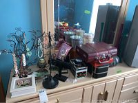 Overview of jewelry stands, jewelry boxes, and decorative items arranged on a wooden dresser against a blue wall.