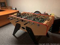 Full side view of the Harvard foosball table showing wooden finish, black legs, and red trim around the playing field.